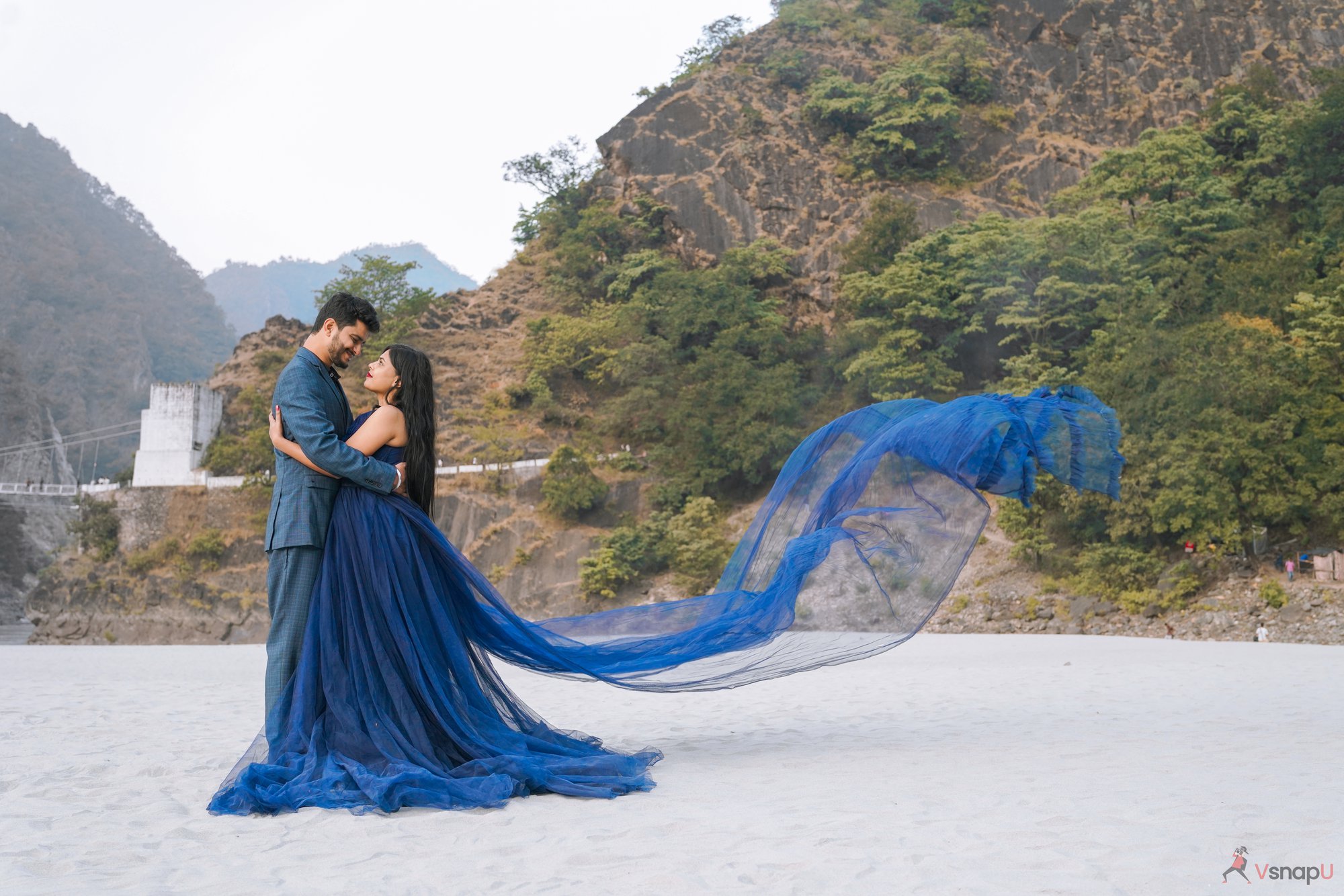 Romantic dance captured in a pre-wedding shoot, with a blue ethnic-dressed couple hugging and looking at each other in an open roof place with mountains behind them.